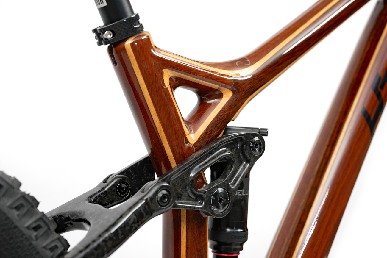 Custom carbon fiber floating linkage and seat stay yoke contrasting Jarrah wood grain of HTech mountain bike frame